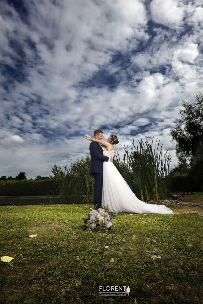 mariage les amoureux se regardent avec tendresse au bord de l'etang et bouquet au premier plan florent studio photographe boulogne sur mer lille le touquet paris saint omer